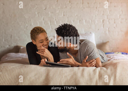 Happy couple talking while using tablet computer on bed at home Stock Photo