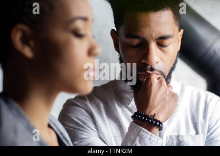 Thoughtful young man with eyes closed by woman at home Stock Photo