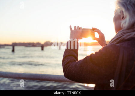 Rear view of senior woman photographing by sea during sunset Stock Photo