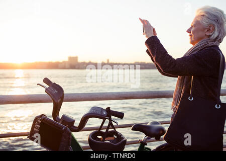 Side view of senior woman photographing during sea sunset Stock Photo