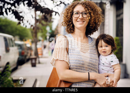 Portrait of smiling mother carrying baby boy while standing on footpath Stock Photo