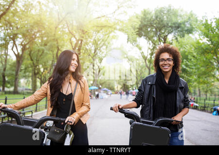 Happy friends talking while walking with bicycle on footpath Stock Photo
