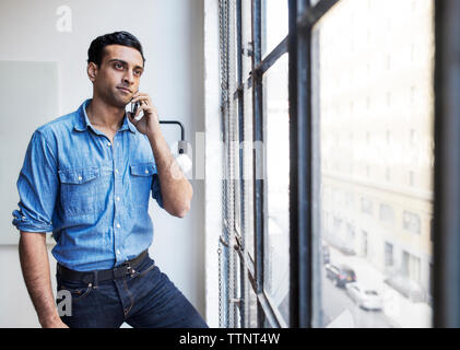 Thoughtful businessman talking on phone in office Stock Photo