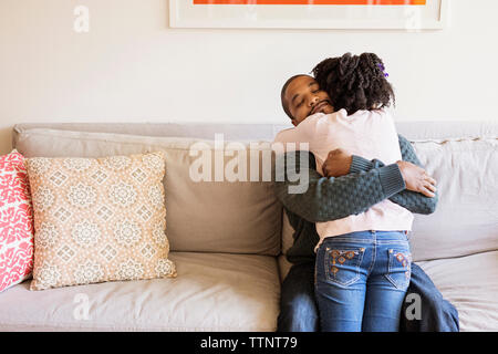 Man embracing daughter while sitting on sofa Stock Photo