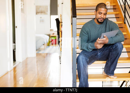 Man using tablet computer while sitting on steps at home Stock Photo