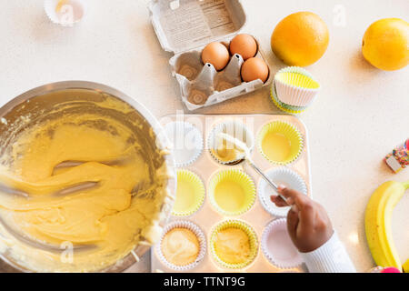 Cropped image of girl filling batter in cupcake holder Stock Photo