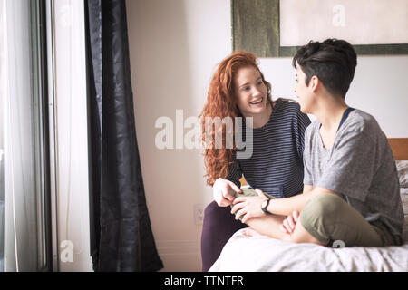Happy couple talking while sitting on bed at home Stock Photo