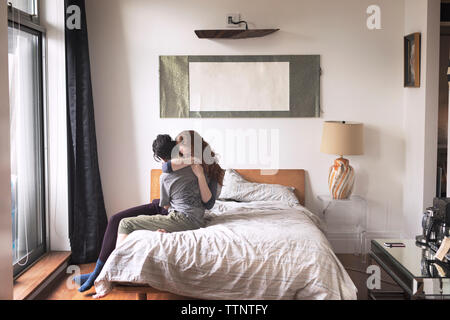 Lesbians embracing while sitting on bed at home Stock Photo