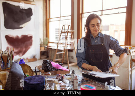 Female artist sticking glass designs on canvas at workshop Stock Photo