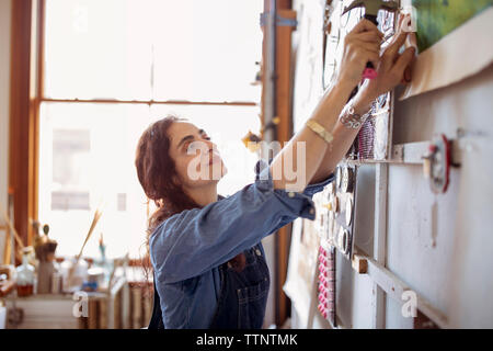 Artist hammering painting on wall in workshop Stock Photo