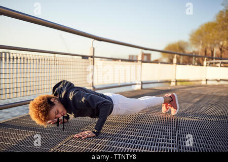 Side view of determined young woman doing push-ups on metallic footpath Stock Photo