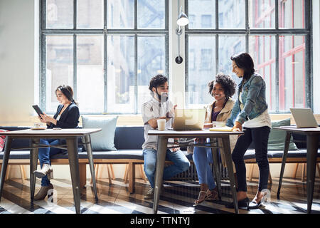 Happy business people discussing while female colleague using tablet computer Stock Photo