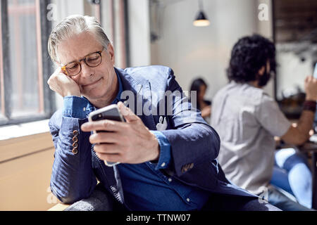 businessman looking at smart phone with male colleague sitting in background Stock Photo