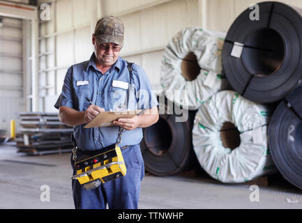 Manual worker writing on clipboard while working in metal Steel industry Factory Stock Photo