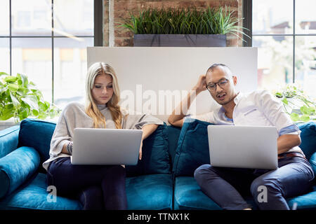 Young business people using laptops while sitting on sofa at creative office Stock Photo