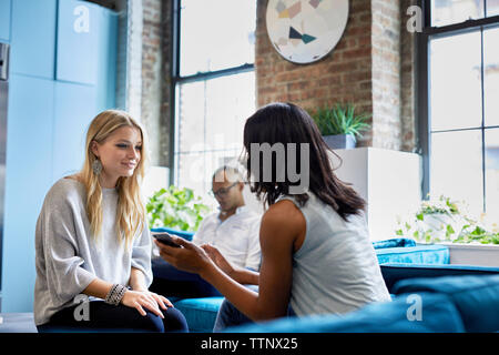 businesswoman discussing over smart phone while male colleague sitting at creative office Stock Photo