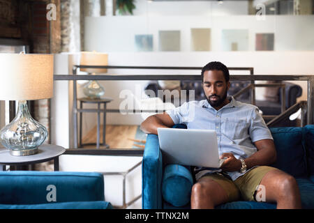 businessman using laptop while sitting on sofa by lamp shade at creative office Stock Photo