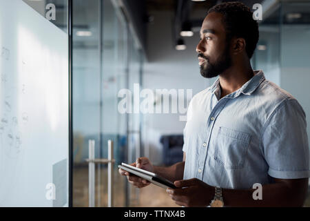 Thoughtful businessman using digital tablet while standing at office corridor Stock Photo