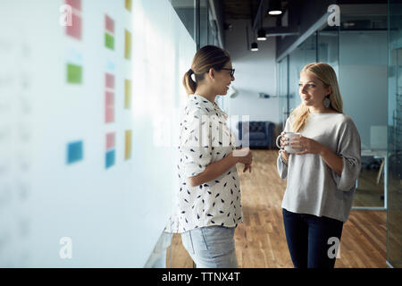 Smiling businesswoman having coffee while listening to colleague standing at corridor Stock Photo