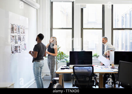 business people looking at photograph printouts on bulletin board while colleagues working in office Stock Photo