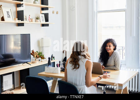 Smiling businesswoman talking with female colleague at desk in office Stock Photo