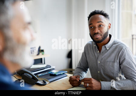 Confident businessman looking at male colleague in office Stock Photo