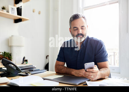 businessman using smart phone while sitting at desk in creative office Stock Photo