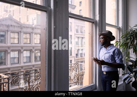 businessman using mobile phone while standing by window in creative office Stock Photo