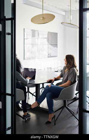 Female colleagues discussing over laptop computer in conference room seen through doorway Stock Photo