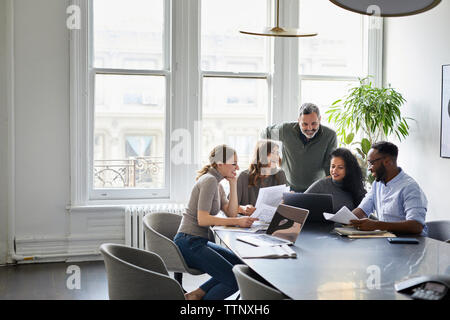 Smiling business people discussing over laptop computer in conference room at creative office Stock Photo