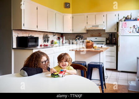 Mother looking at son playing with toys while sitting in kitchen Stock Photo