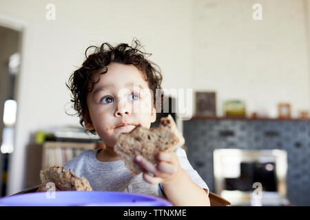 Close-up of cute thoughtful baby boy holding breads while looking away at home Stock Photo
