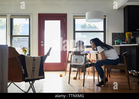 Side view of mother talking with son sitting on chair in living room at home Stock Photo
