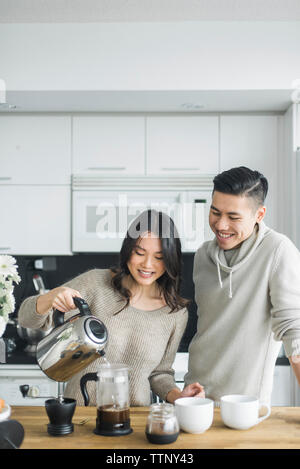 Happy woman with boyfriend making coffee at table in kitchen Stock Photo