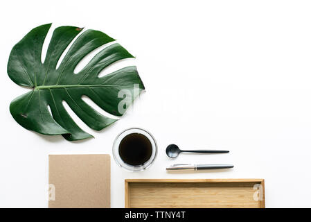 Overhead view of coffee with monstera leaf by wooden tray and office  supplies arranged on white background Stock Photo - Alamy