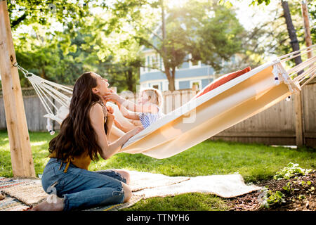 Happy mother playing with daughter sitting in hammock at yard Stock Photo