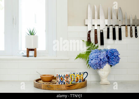 Knives hanging on wall over cups and bowl on kitchen counter Stock Photo