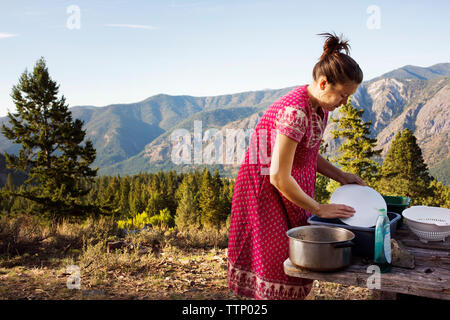 Side view of woman cleaning utensils on mountain Stock Photo