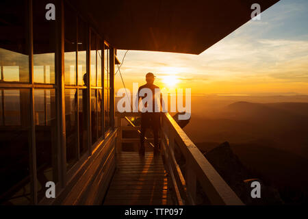 Rear view of hiker standing at fire lookout tower during sunset Stock Photo