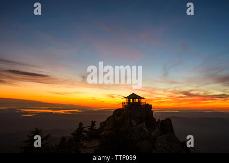 Silhouette fire lookout tower on mountains against sky during sunset Stock Photo