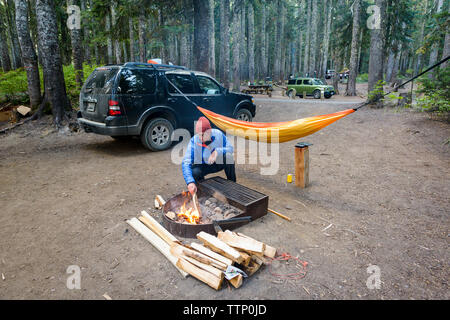 Man preparing fire pit by hammock in forest Stock Photo