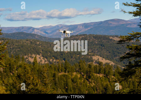 Quadcopter flying over mountains against sky during sunny day Stock Photo