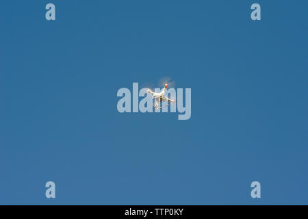 Low angle view of quadcopter flying against clear blue sky during sunny day Stock Photo