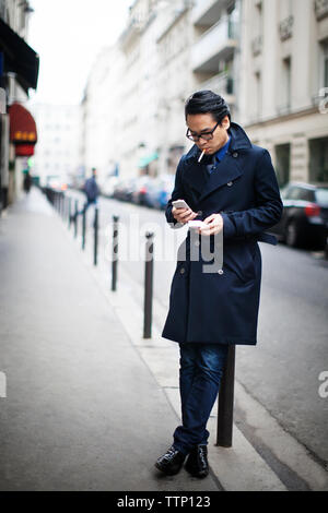 Man using smart phone while leaning on bollard at footpath Stock Photo