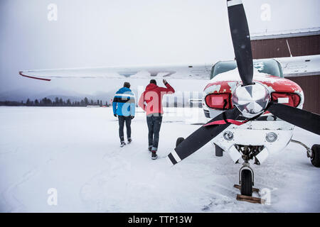 Rear view of men walking by airplane on snow covered field Stock Photo