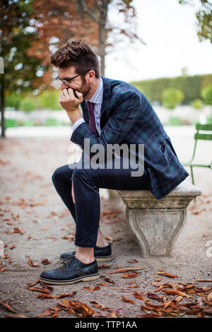 Thoughtful businessman sitting on park bench during autumn Stock Photo