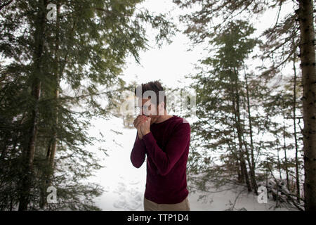 Man warming hands while standing against trees during winter at forest Stock Photo