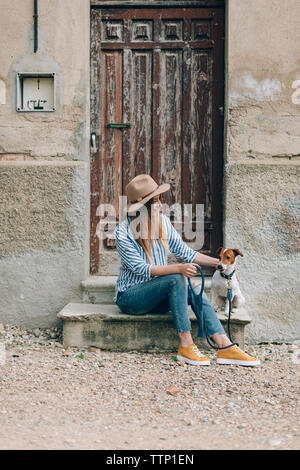 Woman looking at Jack Russell Terrier while sitting on front stoop Stock Photo