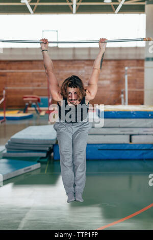 Full length portrait of gymnast hanging on kip at gym Stock Photo