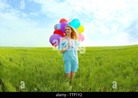 Happy woman with colorful balloons in field on blue sky background Stock Photo